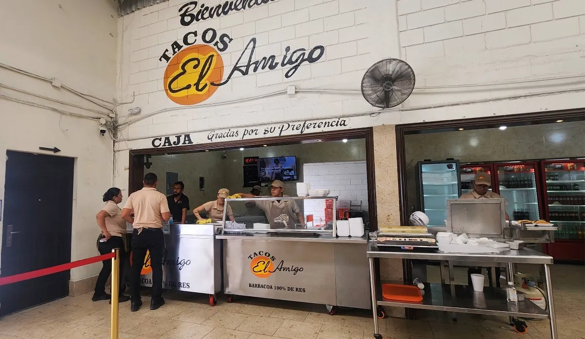Barra de la sucursal Edison, con el logo de Tacos El Amigo sobre la caja y el equipo atendiendo.