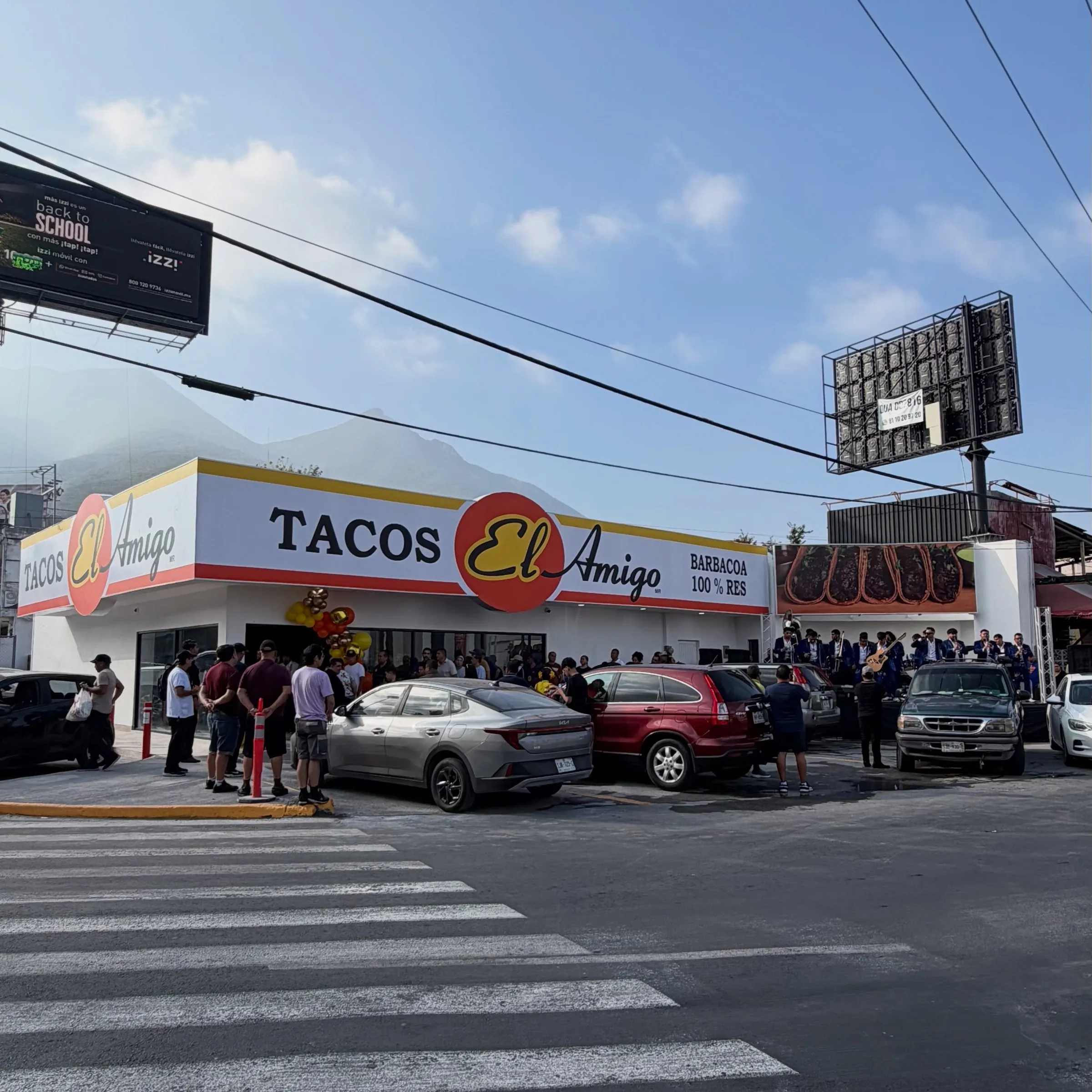 Fachada de una sucursal de Tacos El Amigo el día de su inauguración, con clientes afuera del local.